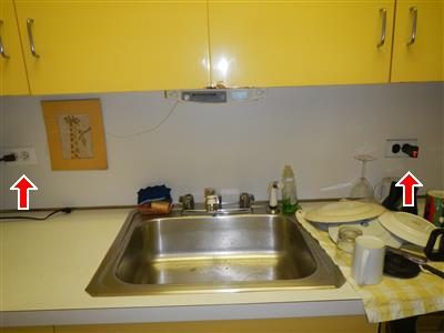 Kitchen counter and stainless sink with wall outlets on both sides marked by red arrows.
