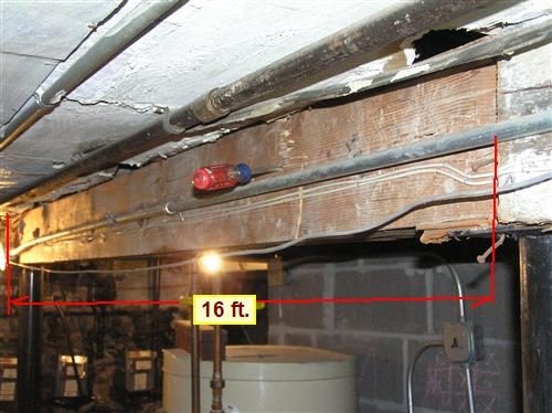 Basement main beam with a screwdriver pushed into the wood and a red bracket marked 16 ft. along its length.