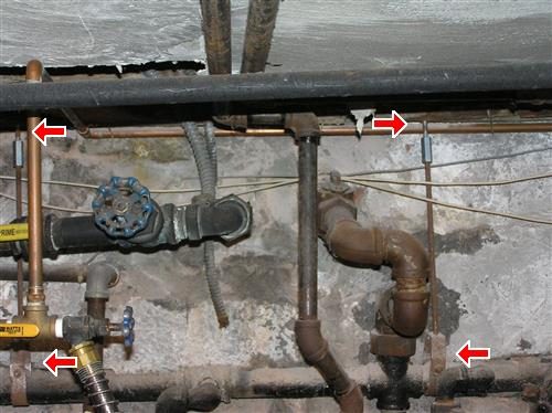 Basement ceiling with black gas piping and valves, four red arrows pointing along the unsupported pipe runs.