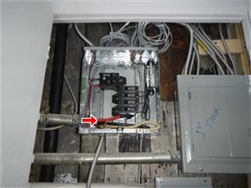 Open sub-panel in a basement with several breakers and a red arrow pointing to the wiring at the bottom.
