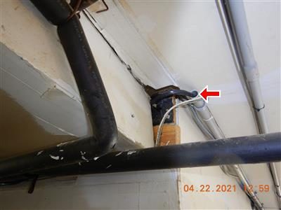 Bare service cable entering a garage ceiling beside black pipes and a conduit end, red arrow at the exit point.