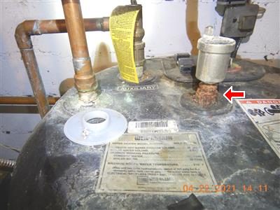 Top of a water heater with copper lines; a heavily corroded pipe coupling is marked with a red arrow.