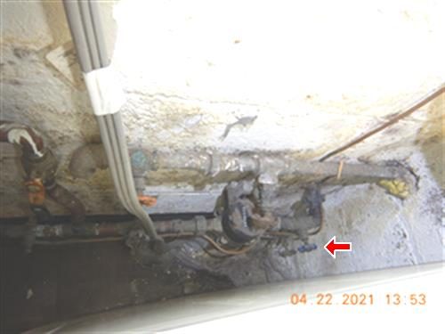 Rusted shut-off valve and piping on a stained foundation wall, water staining below, red arrow at the valve.