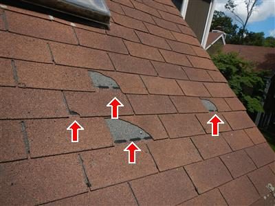 Asphalt shingle roof with several missing shingle pieces marked by four red arrows.