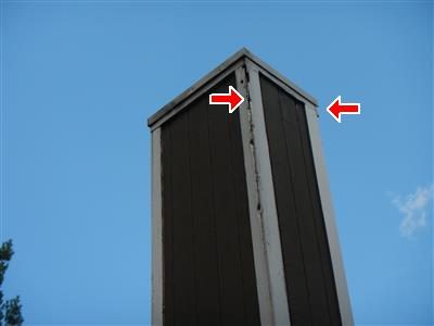 Wood-sided chimney chase against a blue sky with two red arrows at the corner trim near the top.