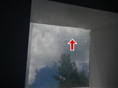 Skylight seen from inside, its glazing covered in small cracks, with a red arrow pointing at them.