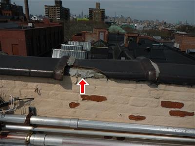 A rooftop parapet with a displaced coping stone arrowed, painted brick spalling below it.