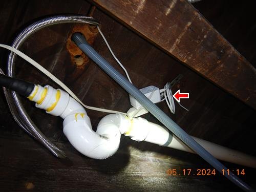 Under-sink plumbing with a flexible corrugated drain line and improvised wiring, one arrow marking the connection.