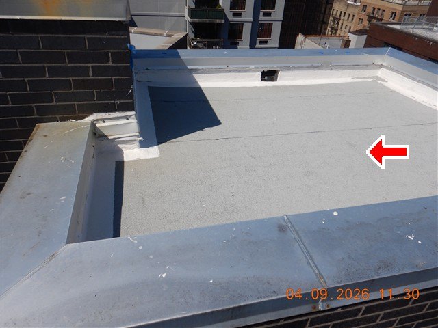 Granular-surfaced flat roof section bordered by metal-capped parapet walls, red arrow, date stamp.