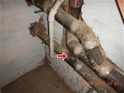 Cast iron drain pipes in a basement corner with a red arrow pointing at an open pipe end.