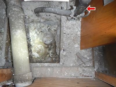 Dusty basement floor pit with old pipes; a red arrow at the top right marks the grey service pipe beneath a wooden step.