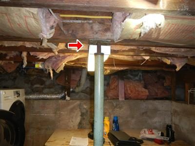 Basement ceiling with a steel screw jack under a main beam, a red arrow at the top of the jack, pink insulation above.