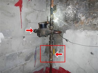 Water meter and copper main shut-off valve on a rough basement wall, marked with a red arrow and red box.