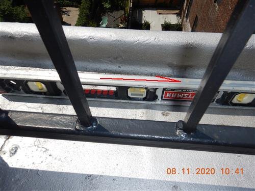 A spirit level held against a rooftop iron railing, with a red line showing the deviation.
