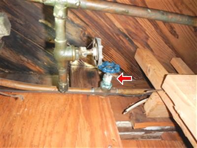 Copper supply pipes at a basement ceiling with a red arrow pointing to a blue-handled valve.
