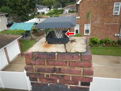 Top of a brick chimney with a stainless steel liner and rain cap, a red arrow pointing to the liner.