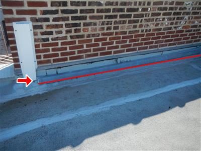 Metal flashing along the base of a brick wall on a flat roof, red line and arrow marking the loose section.