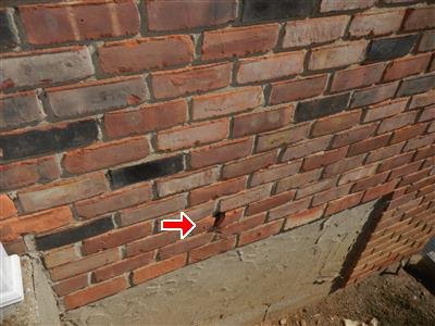 Brick veneer above a concrete foundation with a mortar gap arrowed.