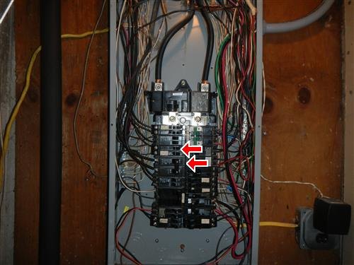 An open electrical panel densely wired, with two arrows marking breaker connections.