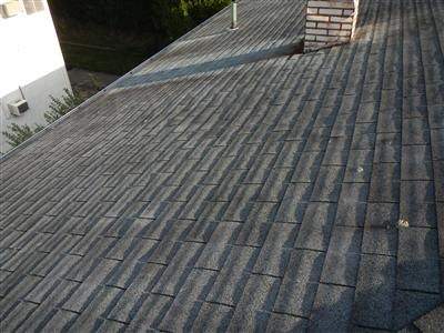 Gray asphalt shingle roof slopes meeting at a valley, with a vent pipe and brick chimney