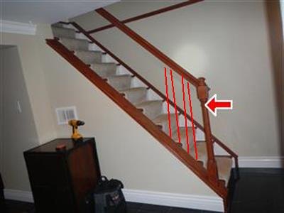 Wood staircase with red lines drawn between balusters and a red arrow at the handrail