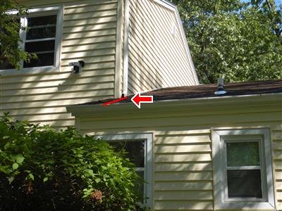 Red arrow at the gutter line where a lower roof meets a yellow-sided upper wall