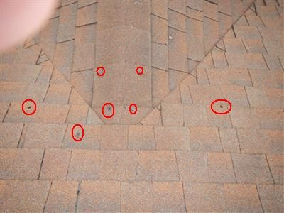 Asphalt shingle roof valley with several red circles around raised nail heads.