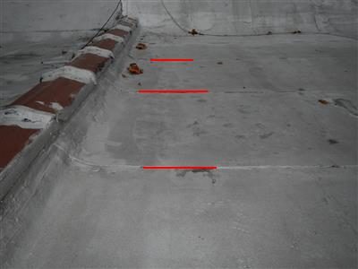 Grey flat roof surface with parapet wall and three short red lines marking lifted seams.