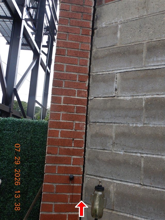 Red brick pier beside a grey concrete block wall with an open vertical joint between them, a red arrow pointing up at the gap.