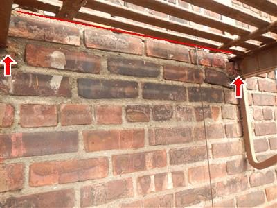 Brick wall under a fire-escape platform with a red line and two red arrows marking loose brickwork at the anchors.