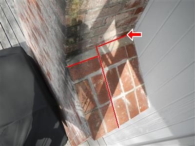 Brick chimney corner beside white siding with red lines tracing cracked mortar joints and a red arrow.