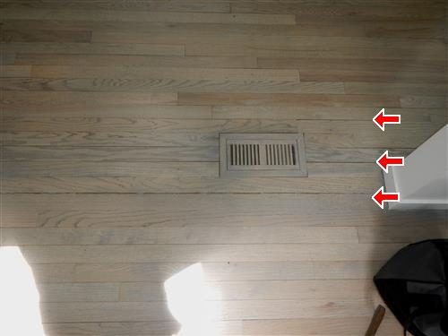 Light hardwood floor around a metal forced-air register, with three red arrows at open board joints.