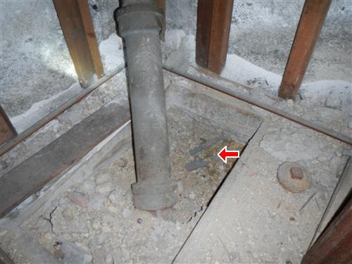A cast iron plumbing stack rising from a rough unfinished floor, debris around its base arrowed.