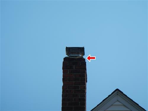 A brick chimney top against a clear sky with an arrow at the cap and screen.
