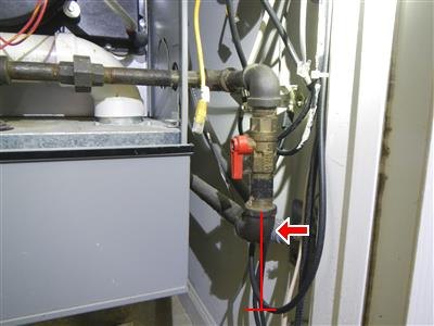 Black iron gas piping with red shutoff valve beside a furnace, red arrow and line at lower pipe