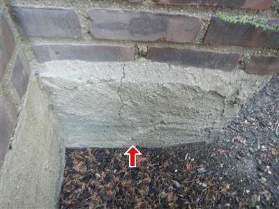 Parged concrete foundation corner below brick, vertical crack, red arrow pointing up at it