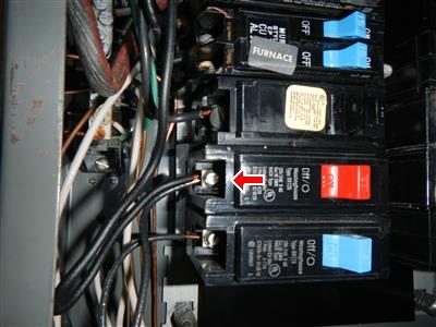Close-up of breakers in an open panel with a red arrow pointing to a terminal holding two wires.