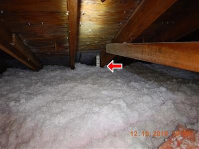 Attic filled with white blown insulation between rafters, a red arrow pointing to a depth gauge reading 16 inches.
