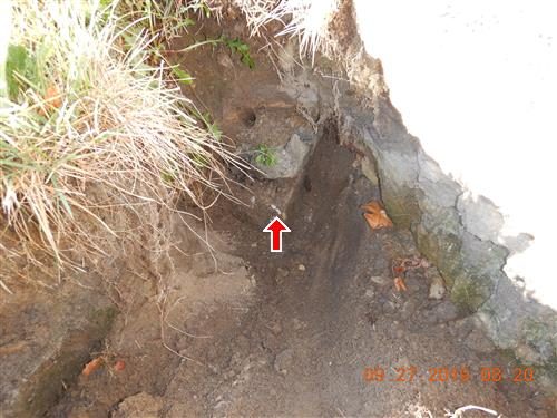 Collapsed soil beside a rubble and brick wall in the ground, with a red arrow pointing into the hole.