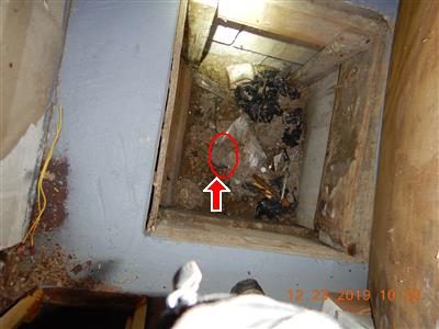 Open floor hatch revealing a dusty pit with debris; a red circle and arrow mark a fitting at the bottom.