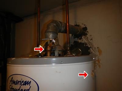 Top of an American Standard water heater with a flue elbow and a valve, two red arrows pointing at the valve and the wall behind.