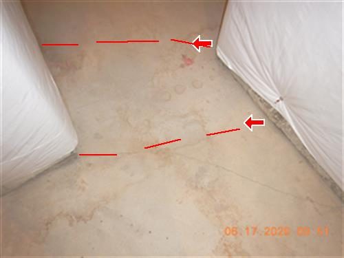 Concrete basement floor between two plastic-wrapped units with red lines tracing a crack and two red arrows.