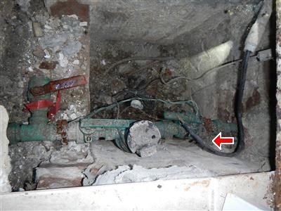Water main pipe in a dusty pit with a red arrow pointing to an unclamped ground cable.