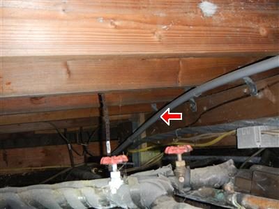 Crawl space ceiling joists with a red arrow pointing to a cable hanging loose above shut-off valves.