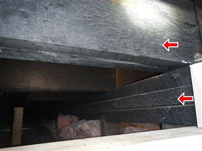 Attic rafters and boards blackened by fire damage, two red arrows.