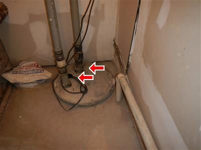 Sewage ejection pump pit in a basement closet with two pipes rising from the lid, red arrows at the cover.