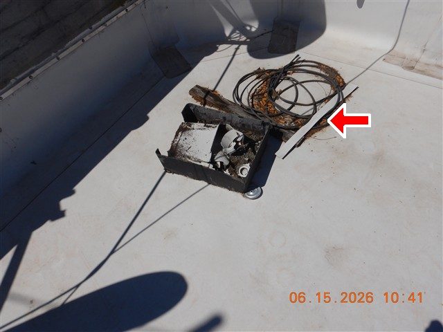 White rubber membrane roof with a coil of cable, a metal box and loose boards left on it, red arrow.