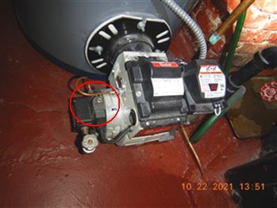 Oil burner assembly mounted on a boiler, red circle around a component, orange date stamp