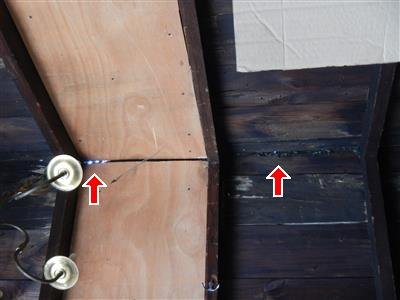 Wood board ceiling and plywood panel with dark staining, two red arrows at stained seams