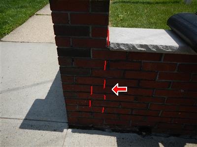 Brick pier of an exterior stoop with mortar joint cracks traced in red, red arrow